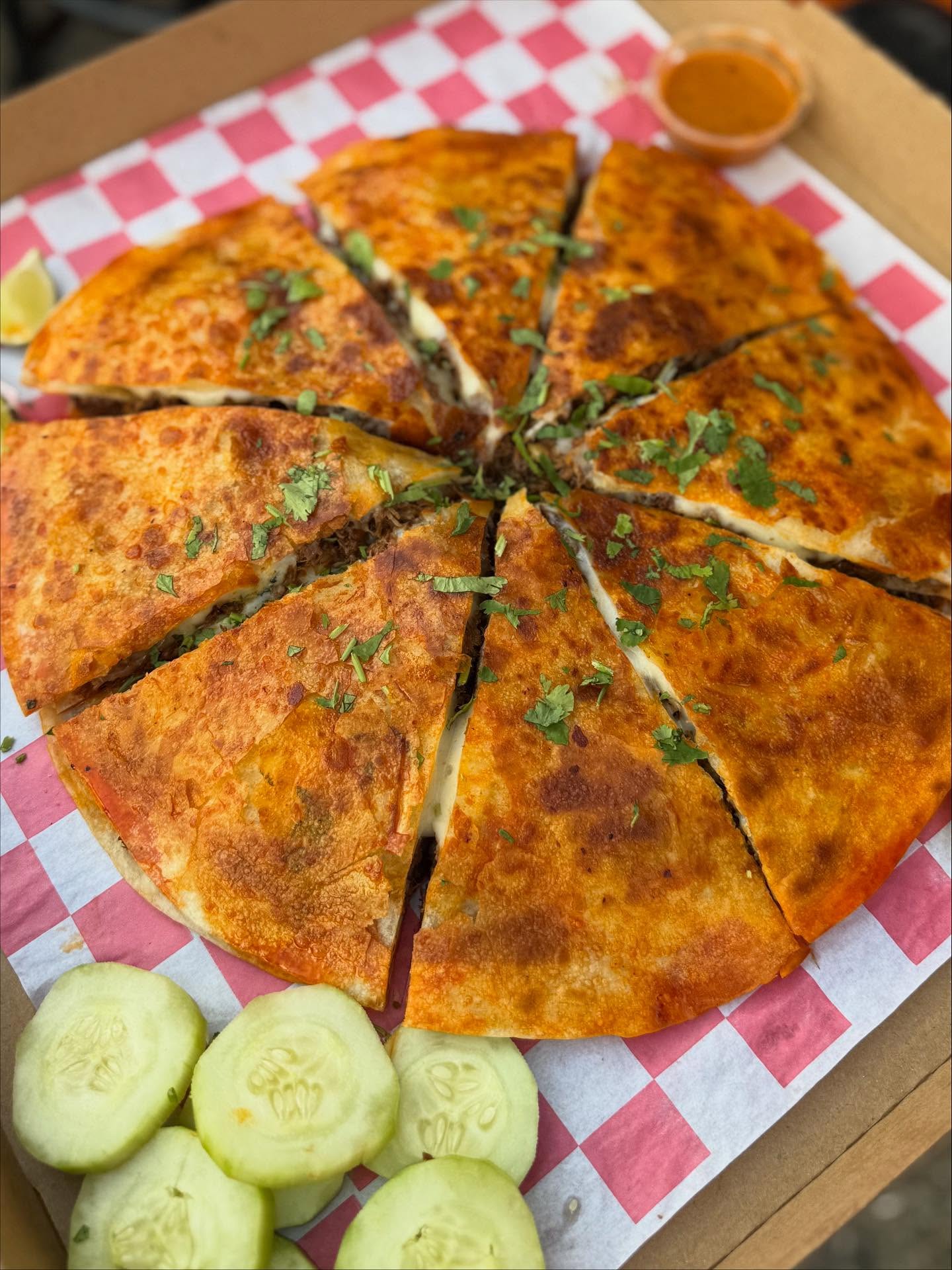 A golden birria quesadilla sliced into wedges with cucumber on the side